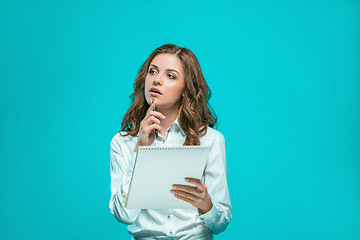 Image showing The thoughtful young business woman with pen and tablet for notes on blue background