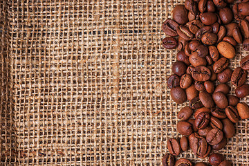 Image showing Black coffee beans in burlap sack on wooden table,