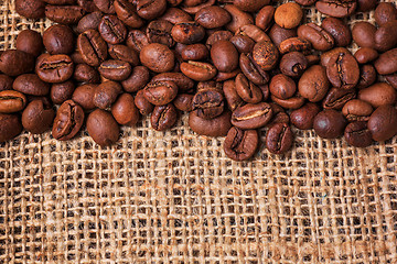 Image showing Black coffee beans in burlap sack on wooden table,