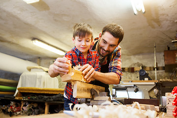 Image showing father and son with plane shaving wood at workshop