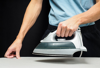 Image showing Male person using a steaming hot iron, on a iron board on black