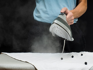 Image showing Male person using a steaming hot iron, on a white shirt