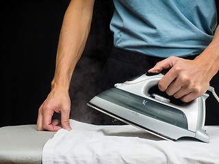 Image showing Male person using a steaming hot iron, on a white shirt