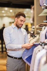 Image showing happy young man choosing clothes in clothing store