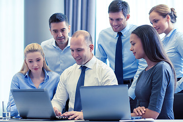 Image showing smiling businesspeople with laptops in office