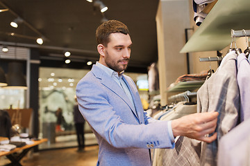 Image showing happy young man choosing clothes in clothing store