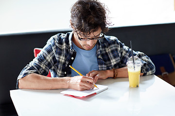 Image showing man with notebook and juice writing at cafe