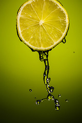 Image showing Juicy lime and drops of juice isolated on green blackground in studio.