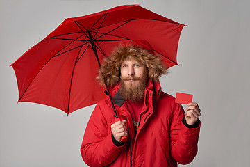 Image showing Man in red winter jacket standing under umbrella and showing blank credit card