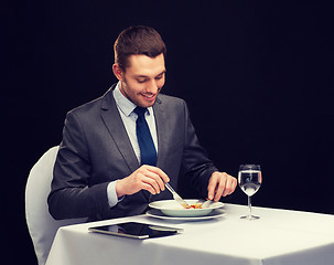 Image showing smiling man with tablet pc eating main course