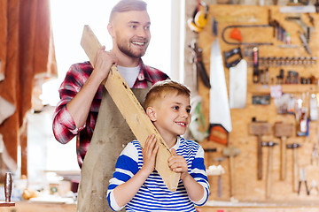 Image showing happy father and son with wood plank at workshop