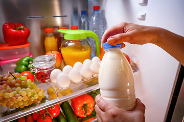 Image showing Woman takes the milk from the open refrigerator