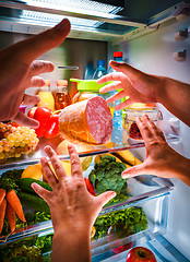 Image showing Human hands reaching for food at night in the open refrigerator