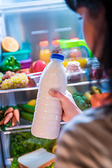 Image showing Woman takes the milk from the open refrigerator