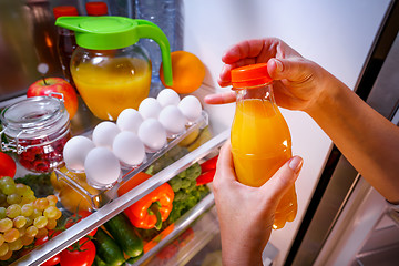 Image showing Woman takes the Orange juice from the open refrigerator