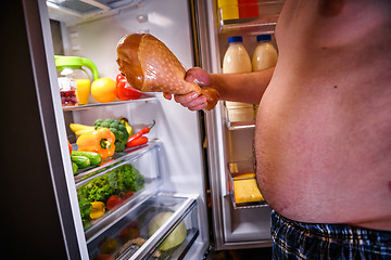 Image showing Hungry man holding a turkey leg in his hands and standing next t