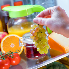 Image showing Woman takes the bunch of grapes from the open refrigerator