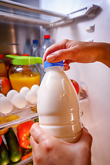 Image showing Woman takes the milk from the open refrigerator