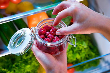 Image showing Woman takes the fresh raspberries from the open refrigerator