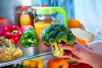 Image showing Woman takes the broccoli from the open refrigerator.