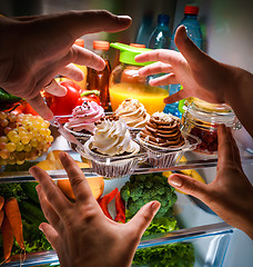 Image showing Human hands reaching for sweet cake at night in the open refrige