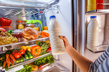 Image showing Woman takes the milk from the open refrigerator