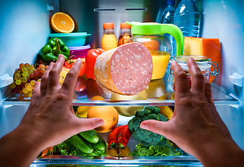 Image showing Human hands reaching for food at night in the open refrigerator