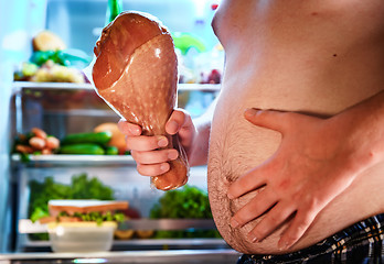 Image showing Hungry man holding a turkey leg in his hands and standing next t