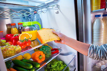 Image showing Woman takes the piece of cheese from the open refrigerator