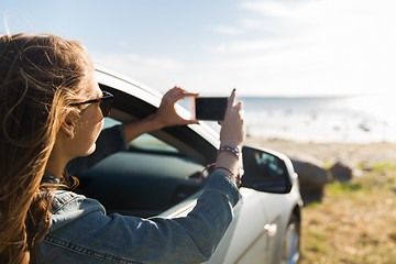 Image showing happy young woman in car with smartphone at sea