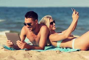 Image showing happy couple with modern gadgets lying on beach