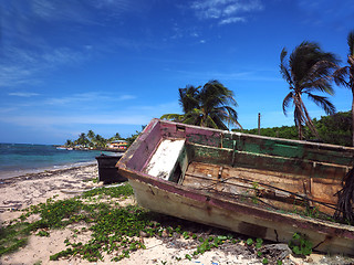 Image showing wooden fishing boat rotting on beach with hotel in background No