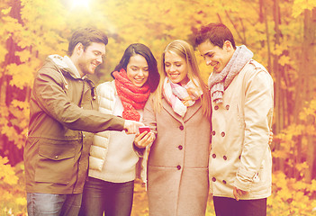 Image showing smiling friends with smartphones in city park