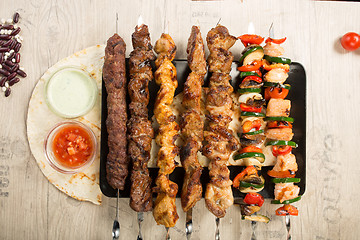 Image showing set shashlik. kebab skewer, black rectangular plate. sauce and onions