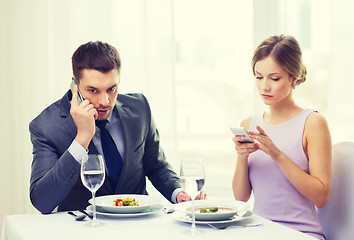 Image showing busy couple with smartphones at restaurant