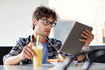 Image showing man with tablet pc and earphones sitting at cafe