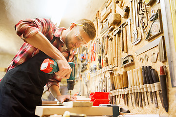 Image showing carpenter with drill drilling plank at workshop