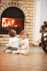 Image showing The two little girls sitting at home against fireplace