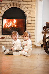 Image showing The two little girls sitting at home against fireplace