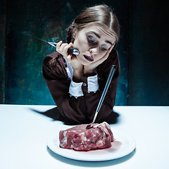 Image showing Bloody Halloween theme: crazy girl with a knife, fork and meat