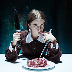 Image showing Bloody Halloween theme: crazy girl with a knife, fork and meat