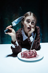 Image showing Bloody Halloween theme: crazy girl with a knife, fork and meat