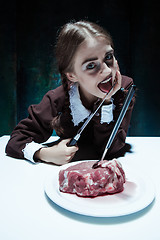 Image showing Bloody Halloween theme: crazy girl with a knife, fork and meat