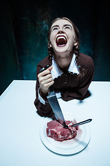 Image showing Bloody Halloween theme: crazy girl with a knife, fork and meat