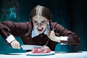 Image showing Bloody Halloween theme: crazy girl with a knife, fork and meat