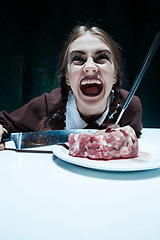 Image showing Bloody Halloween theme: crazy girl with a knife, fork and meat