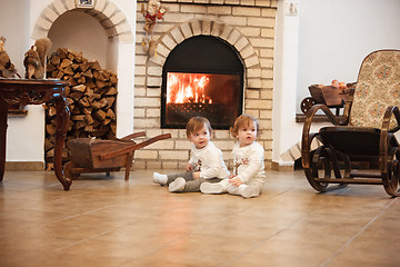 Image showing The two little girls sitting at home against fireplace