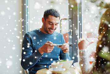 Image showing happy couple picturing food by smartphone at cafe