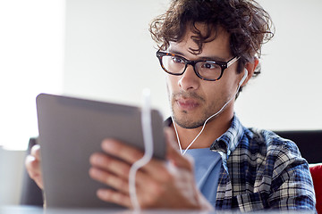 Image showing man with tablet pc and earphones sitting at cafe