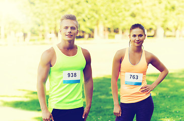 Image showing happy friends or couple with racing badge numbers